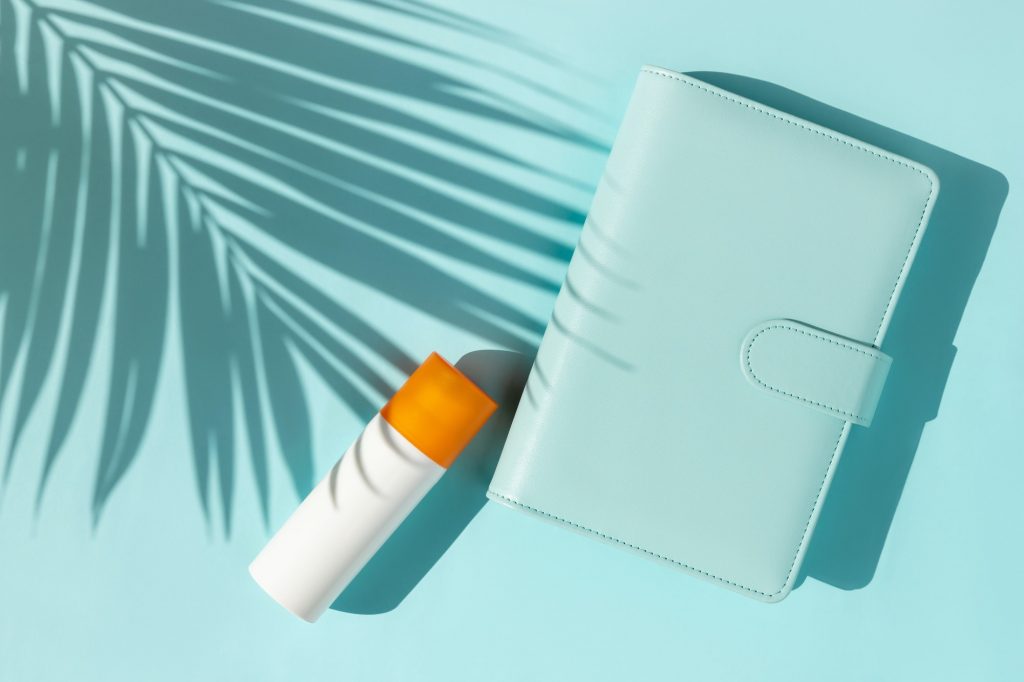 Bottle of sunscreen and notepad with palm leaf shadow on blue background