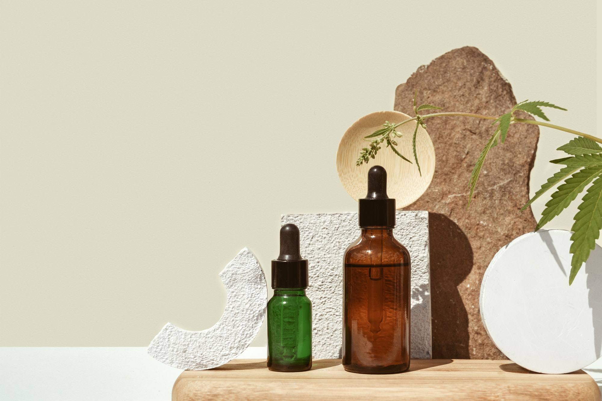 Various glass bottles with CBD oil, THC tincture and hemp leaves on beige background. minimalism